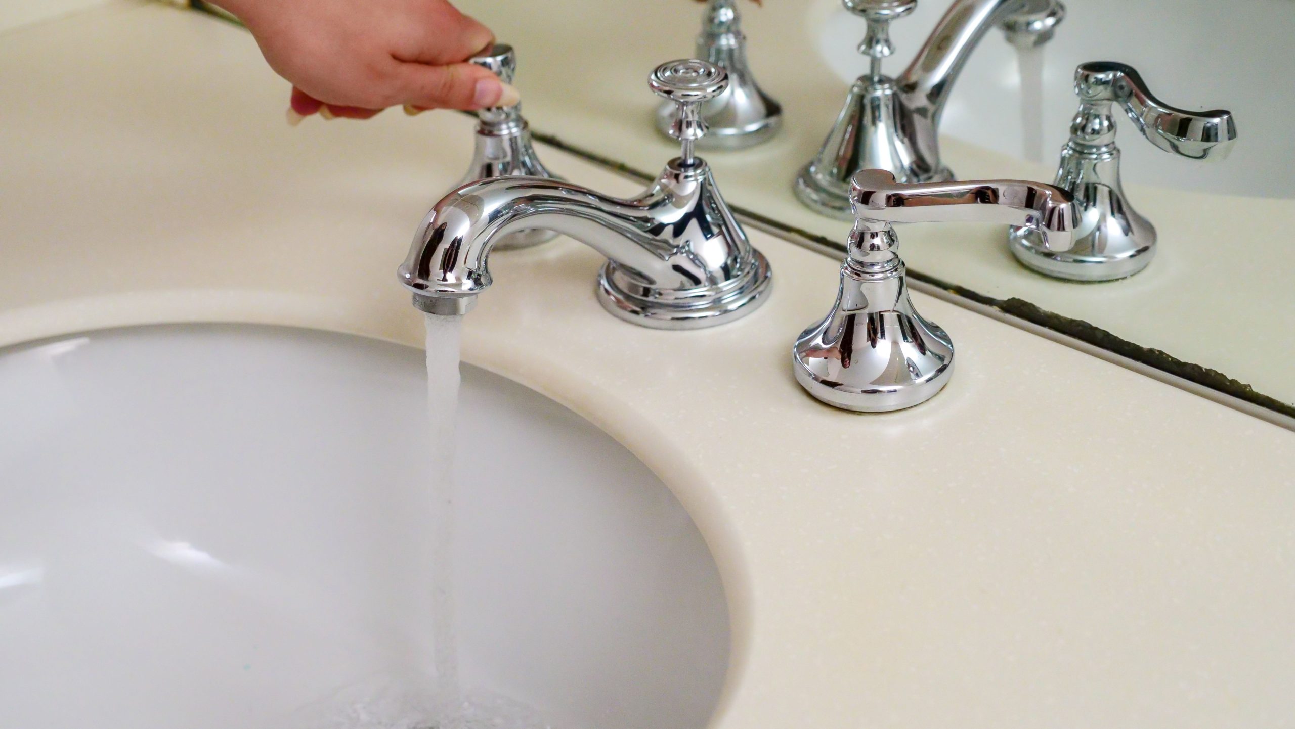 Main actionnant un robinet chrome avec eau courante